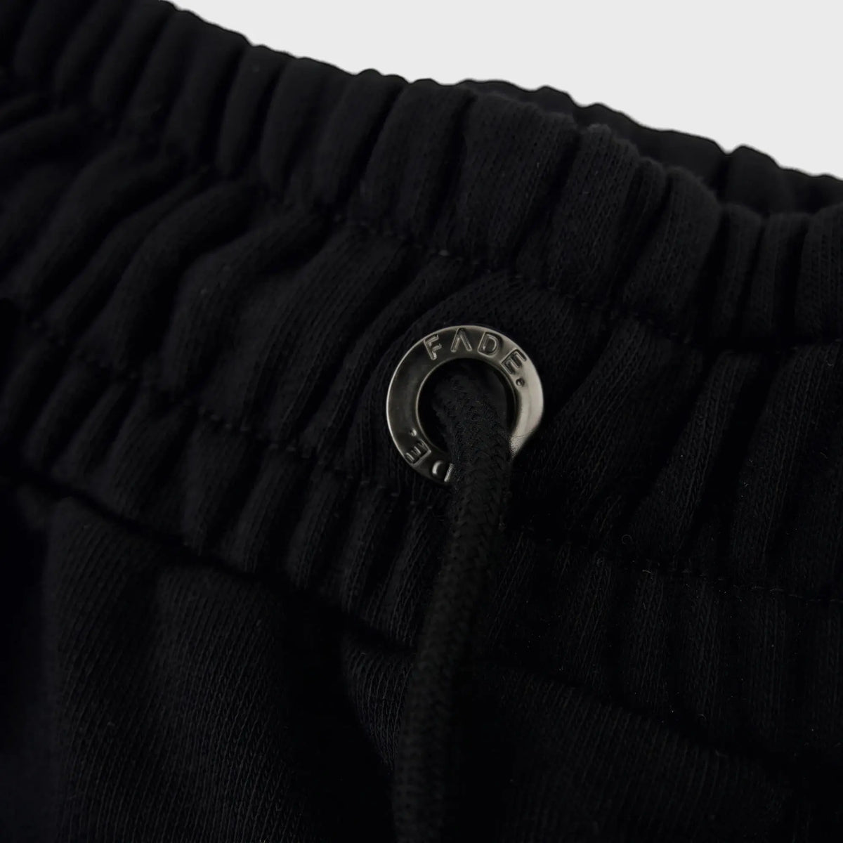 Close-up of the black FJ033 Iconic Badge Shorts waistband, featuring an elasticated design, black drawstring, and a metallic