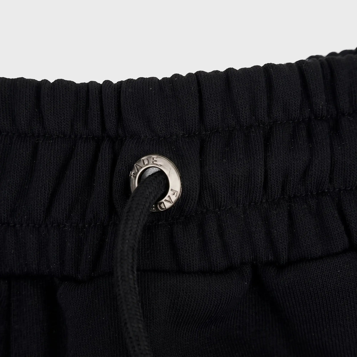 Close-up of black FJ033 Iconic Badge Shorts, featuring an elastic waistband with a black drawstring and a silver branded